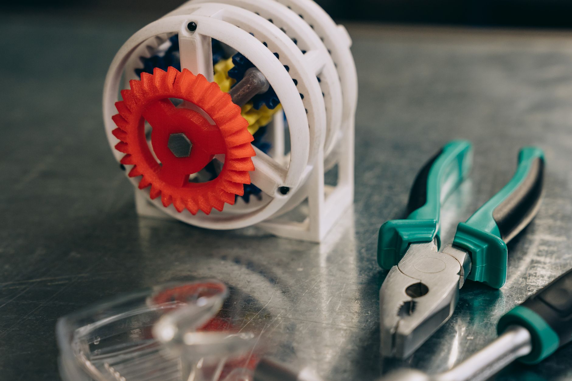 A 3D-printed gear mechanism alongside tools on a metal surface.