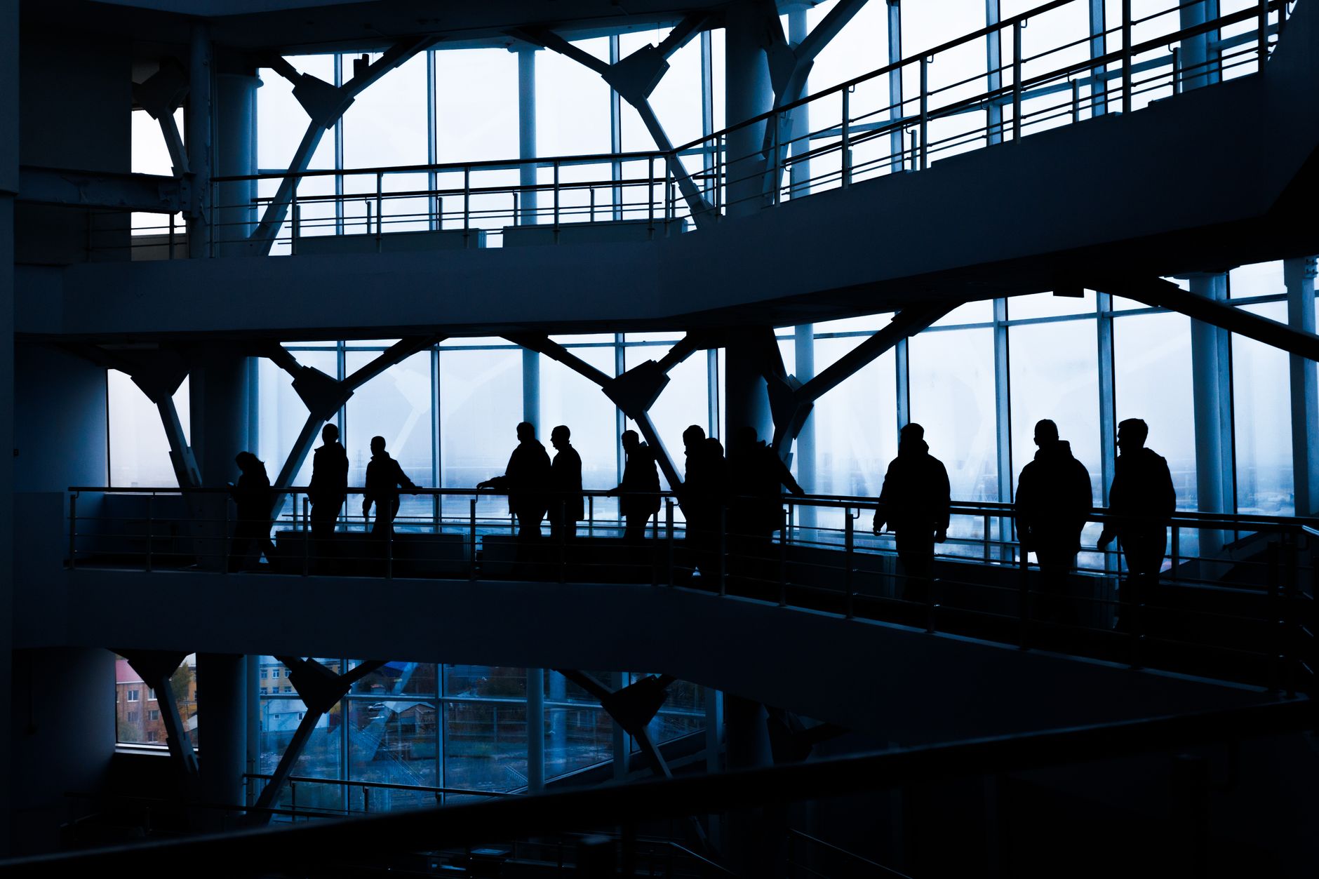 Silhouettes of people walking in a modern architectural building with large windows. — How IPTV Enhances the Viewing Experien